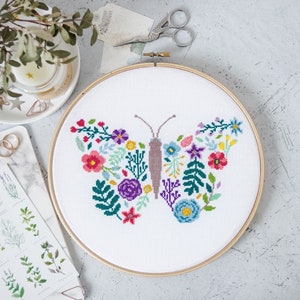 May include: A white embroidery hoop with a colorful floral butterfly design. The butterfly is made up of various flowers and leaves in shades of pink, red, purple, blue, green, and yellow.