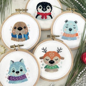 May include: Five embroidered hoop ornaments featuring winter animals wearing scarves. The animals are a penguin, a walrus, a polar bear, a reindeer, and a wolf. The hoops are all wooden and have a white background.