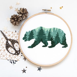 Puede incluir: Un aro de bordado de punto de cruz con un dise&ntilde;o verde y blanco de una silueta de oso con un bosque en su interior. El oso est&aacute; mirando hacia la derecha y caminando.