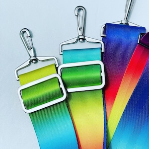 Könnte beinhalten: Drei Regenbogen-Ombre-Stoffbänder mit silbernen Metallschließen. Die Bänder sind grün, blau, gelb, orange, rot und lila.