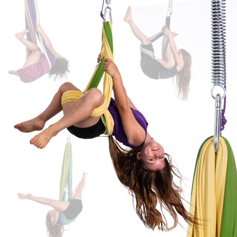 K&ouml;nnte beinhalten: Eine junge Person h&auml;ngt kopf&uuml;ber in einer gelb-gr&uuml;nen Aerial-Yoga-Schaukel. Die Schaukel ist an einer Metallfeder und einem silbernen Karabiner befestigt. Weitere Aerial-Yoga-Schaukeln sind im Hintergrund zu sehen.