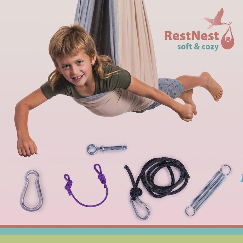 Puede incluir: Un ni&ntilde;o est&aacute; suspendido en una hamaca beige y gris, con el texto "RestNest soft & cozy". Debajo hay varios componentes de hardware: un mosquet&oacute;n, una cuerda morada, una cuerda negra con un mosquet&oacute;n, un resorte y un perno de ojo de metal.