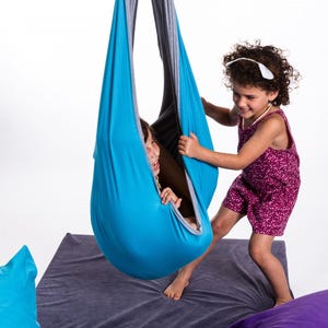 Girls playing with light blue restNest sensory swing chair, indoor hammock swing, Montessori-inspired kids room decor made from soft cotton fabric for sensory regulation and cosy relaxation.