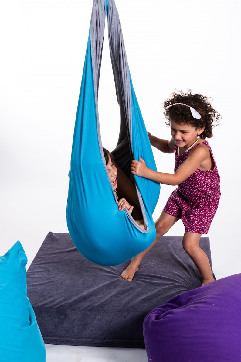 Girls playing with light blue restNest sensory swing chair, indoor hammock swing, Montessori-inspired kids room decor made from soft cotton fabric for sensory regulation and cosy relaxation.