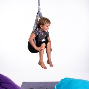 Boy sitting in restNest sensory swing chair with spring suspension, indoor hammock swing, Montessori-inspired kids room decor made from soft cotton fabric for sensory regulation and cosy relaxation.