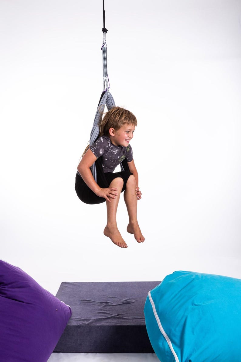 Boy sitting in restNest sensory swing chair with spring suspension, indoor hammock swing, Montessori-inspired kids room decor made from soft cotton fabric for sensory regulation and cosy relaxation.