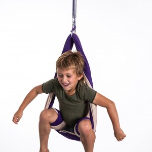 Boy sitting in restNest sensory swing chair with spring suspension, indoor hammock swing, Montessori-inspired kids room decor made from soft cotton fabric for sensory regulation and cosy relaxation.