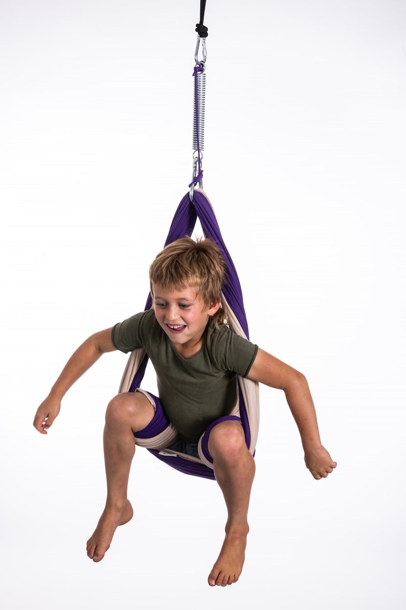 Boy sitting in restNest sensory swing chair with spring suspension, indoor hammock swing, Montessori-inspired kids room decor made from soft cotton fabric for sensory regulation and cosy relaxation.