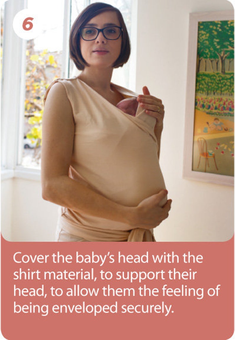 May include: A beige baby wrap carrier. The carrier is being used to hold a baby. The text in the image says to cover the baby's head with the shirt material to support their head, allowing them to feel enveloped securely.
