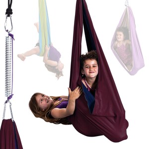 Girls play in plum color restNest sensory swing chair with spring suspension, indoor hammock swing, Montessori-inspired kids room decor made from soft cotton fabric for sensory regulation and cosy relaxation.