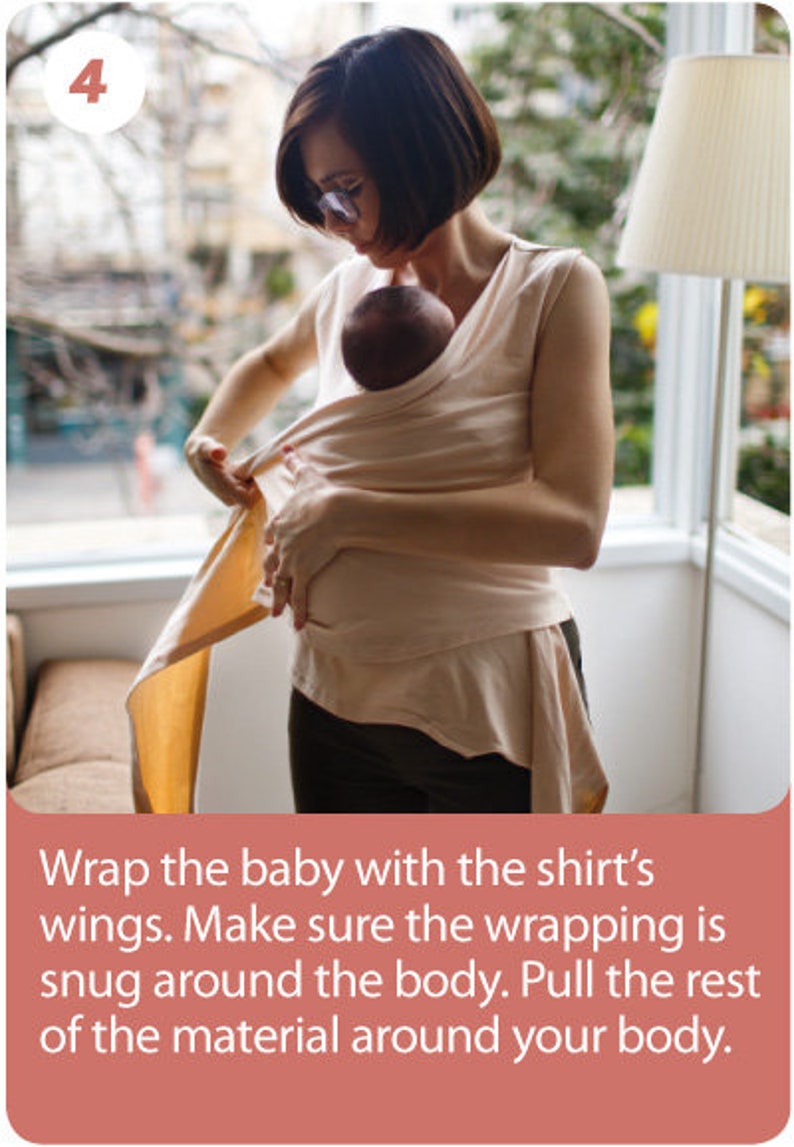 May include: A person wearing a light beige baby wrap, holding a baby. The wrap is being secured around the baby's body. The image includes text that reads: "Wrap the baby with the shirt's wings. Make sure the wrapping is snug around the body. Pull the rest of the material around your body."