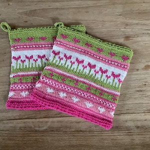 Könnte beinhalten: Zwei gehäkelte Topflappen mit einem rosa, grünen und weißen Blumenmuster. Die Topflappen haben eine Schlaufe zum Aufhängen.