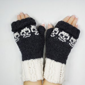 Puede incluir: Un par de guantes sin dedos negros con un patrón de calavera blanca y puños de punto blanco.