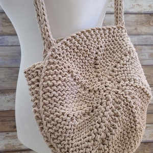 May include: A beige crocheted tote bag with a round, circular shape and two long straps. The bag is made of a thick, textured yarn.