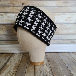 May include: Black and white houndstooth knit headband on a mannequin head.