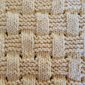 May include: A close-up of a knitted fabric with a woven pattern. The fabric is a light yellow color and has a soft, textured surface.