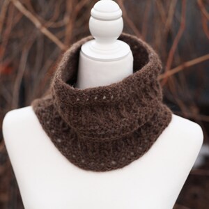 May include: A brown crocheted cowl neck warmer on a white mannequin. The cowl is made with a stitch pattern that creates a textured look.