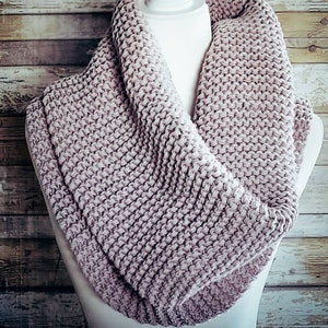 May include: A soft, mauve knitted infinity scarf. The scarf is made of a chunky yarn and has a simple, textured stitch pattern.