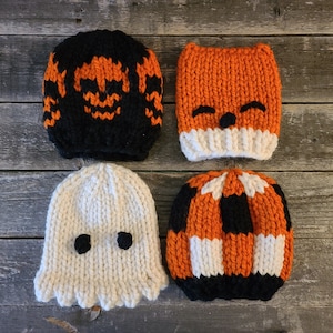Könnte beinhalten: Vier gestrickte Halloween-Mützen in Orange, Schwarz und Weiß. Die Mützen zeigen einen Kürbis, einen Fuchs, ein Gespenst und ein gestreiftes Muster.