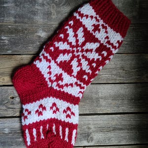 May include: A red and white knitted Christmas stocking with a snowflake pattern. The stocking is hanging on a wooden surface.