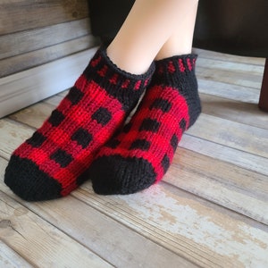 May include: A pair of black and red knit socks with a buffalo plaid pattern. The socks are ankle-length and have a ribbed cuff.