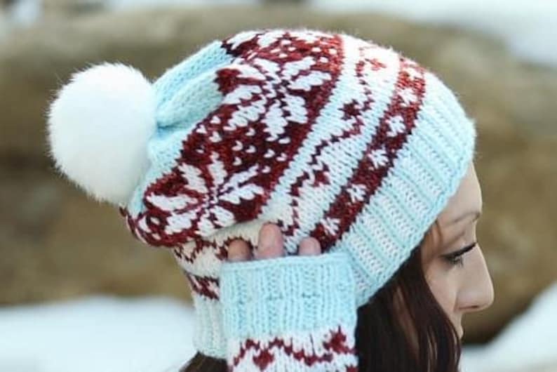 May include: A blue and white knitted hat with a red and white patterned design. The hat has a white pom-pom on top.