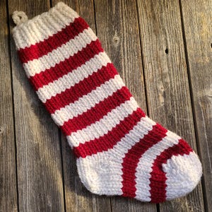 Könnte beinhalten: Ein rot-weiß gestreifter, gestrickter Weihnachtssocken.