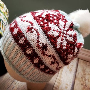 May include: A knitted winter hat with a white pom pom. The hat has a red and white pattern with a light blue base.