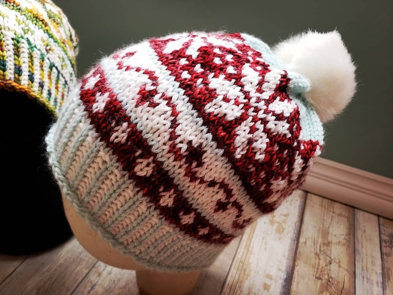 May include: A knitted winter hat with a white pom pom. The hat has a red and white pattern with a light blue base.