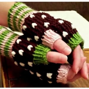 May include: Hand-knitted fingerless gloves in shades of brown, green, pink, and white. The gloves feature a brown body with white heart-shaped accents, green and pink striped cuffs, and pink finger openings. The gloves are designed to keep hands warm while leaving fingers free.
