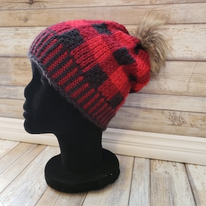 May include: Red and black plaid knit beanie with a faux fur pom pom on top.