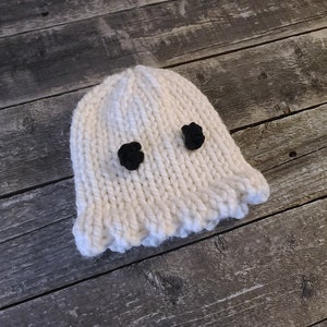 May include: White knitted ghost hat with black felt eyes. The hat has a ruffled edge.