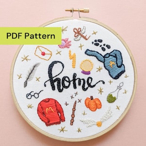 May include: Embroidered hoop art with a white background and a variety of colorful stitched images. The word "home" is stitched in black script. Other images include a sweater, glasses, a wand, and a pumpkin. The text "PDF Pattern" is in a green rectangle.
