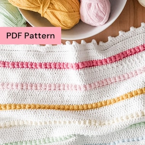 May include: A white crocheted blanket with colorful horizontal stripes in pink, yellow, and blue. The blanket has a textured, bobble stitch design. The image also shows balls of yarn in various pastel colors, and the text "PDF Pattern".