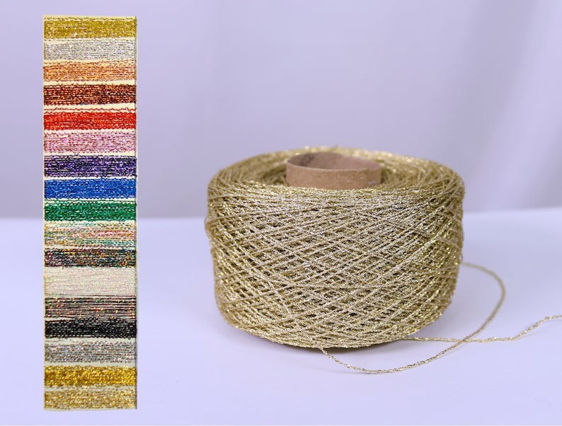 May include: A large spool of gold metallic yarn is displayed beside a colour chart of various metallic threads. The yarn is wound around a cardboard core. The colour chart shows a range of colours, including gold, silver, red, and blue, suitable for crafting and embellishments.