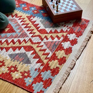 May include: A red, yellow, and blue patterned rug with fringe on the edges. A wooden chessboard with chess pieces is on top of the rug.