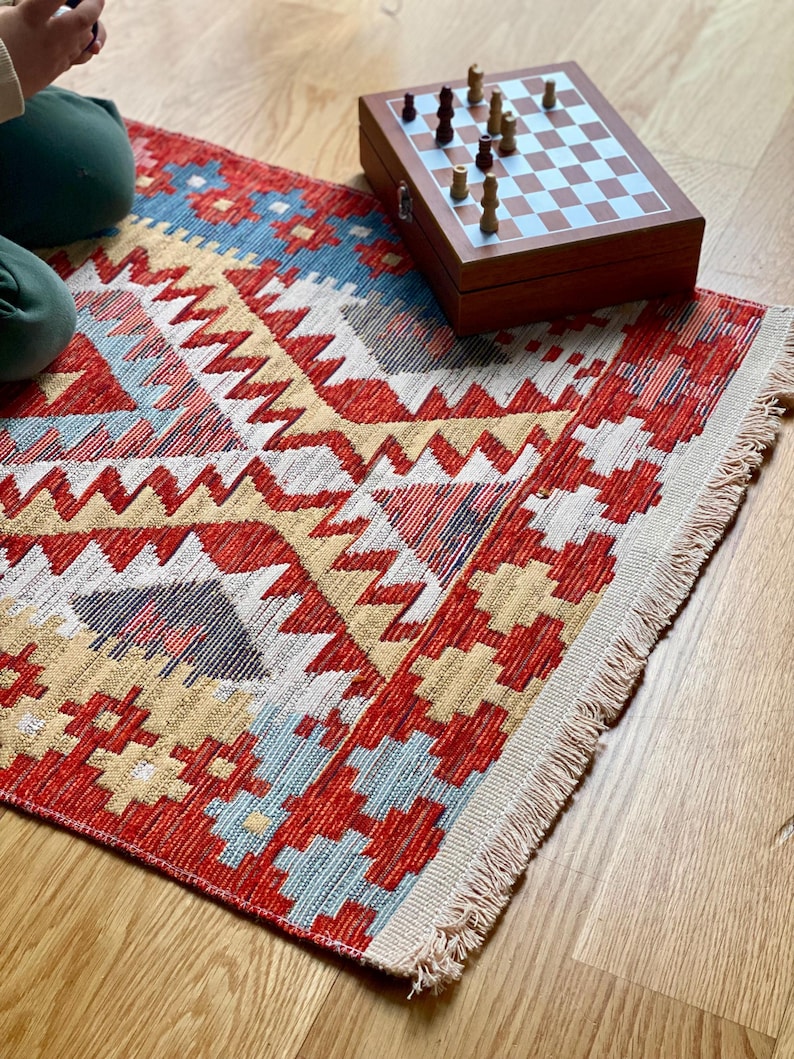 May include: A red, yellow, and blue patterned rug with fringe on the edges. A wooden chessboard with chess pieces is on top of the rug.