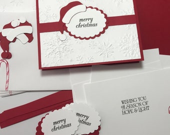 Puede incluir: Una tarjeta blanca con un borde rojo y un diseño de copo de nieve rojo. La tarjeta tiene un círculo blanco con el texto "merry christmas" en negro. Hay dos círculos blancos con el texto "merry christmas" en negro sobre un fondo rojo.