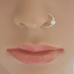 May include: A gold nose ring with a white opal bead. The ring is made of wire and has a simple design.