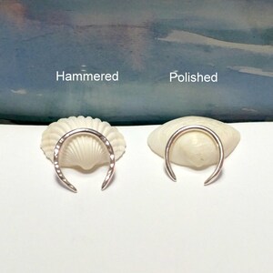 K&ouml;nnte beinhalten: Zwei silberne Ringe, einer geh&auml;mmert und einer poliert, auf Muscheln pr&auml;sentiert. Die Ringe haben beide die Form eines Halbmondes.