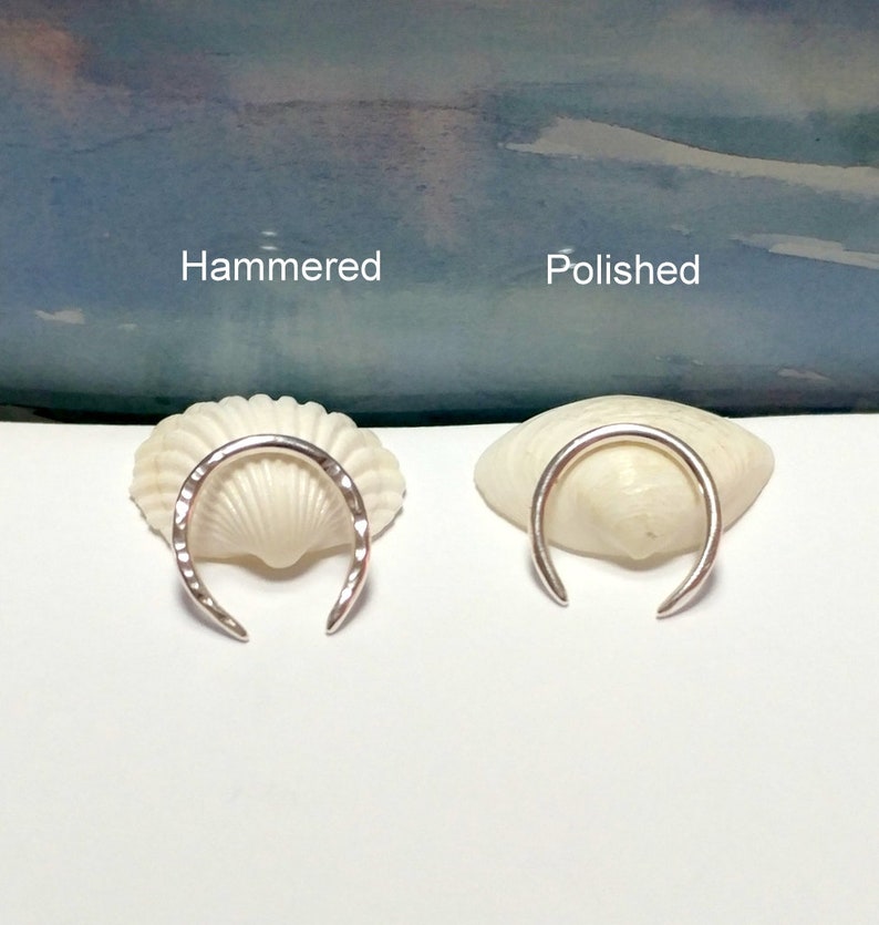 K&ouml;nnte beinhalten: Zwei silberne Ringe, einer geh&auml;mmert und einer poliert, auf Muscheln pr&auml;sentiert. Die Ringe haben beide die Form eines Halbmondes.