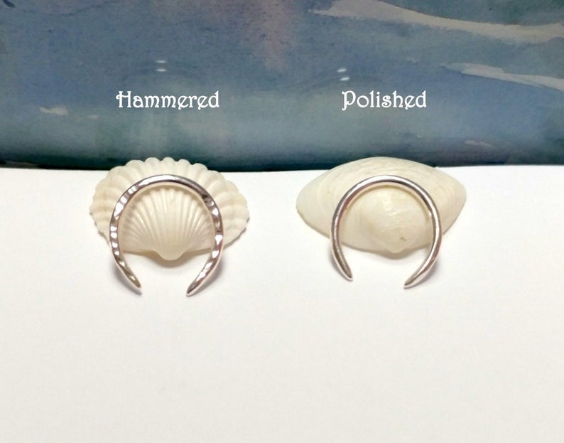 K&ouml;nnte beinhalten: Zwei silberne Ringe, einer geh&auml;mmert und einer poliert, werden auf Muscheln pr&auml;sentiert. Die Ringe sind beide halbkreisf&ouml;rmig und haben spitze Enden.