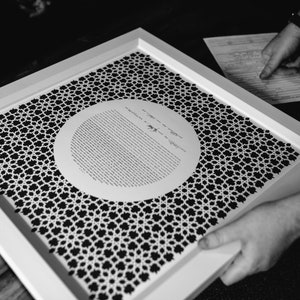 May include: A white framed document with a black and white geometric pattern. The document has a circle in the center with text in Hebrew.