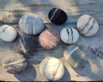 May include: A collection of ten felt stones in various colors and patterns, including gray, white, black, brown, and pink. The stones are arranged on a wooden surface.