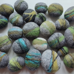 Op de afbeelding: Een verzameling viltballen in verschillende tinten groen, grijs en blauw. De ballen hebben een marmerpatroon met strepen en swirls.