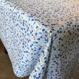 May include: White tablecloth with a blue and green floral pattern. The tablecloth is made of a soft, woven fabric and has a subtle sheen.