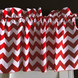 May include: Red and white chevron patterned valance with a white ruffle top and a white bottom edge. The valance is hanging on a silver curtain rod.