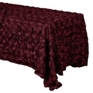 May include: Burgundy rose satin tablecloth with a textured, ruffled design. The tablecloth is made of soft, luxurious fabric and is perfect for adding a touch of elegance to any event.