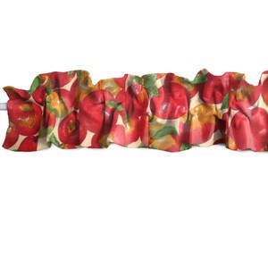 May include: A ruffled valance featuring a repeating pattern of red apples with green leaves and yellow highlights on a cream background. The fabric is gathered and draped, creating a textured effect. The valance is designed for a window treatment.