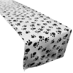 May include: A white table runner with a black paw print pattern. The runner is made of a soft, silky fabric and is perfect for adding a touch of whimsy to any table setting.